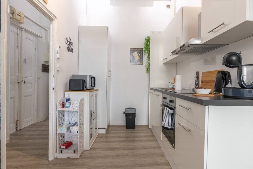 Een smalle keuken met witte kastjes, een magnetron, een koffieapparaat en een prullenbak.