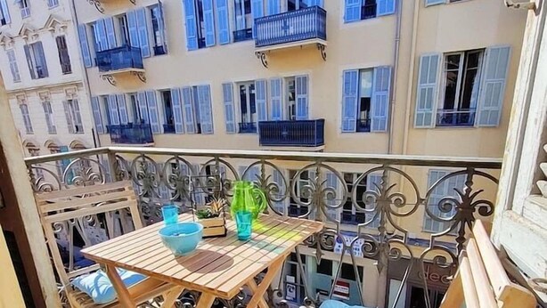 A balcony with a wooden table and chairs, a blue cushion, and a green bottle.