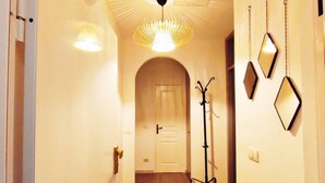 A hallway with a door at the end, a hanging light fixture, and a coat rack with mirrors.