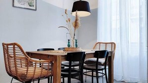 A dining area with a wooden table, four chairs, a vase with dried plants, and a lamp.