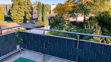 A rooftop terrace with a metal railing, a green carpet, and a view of surrounding buildings and trees.