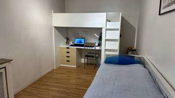 Ein kleines Zimmer mit einem Etagenbett, einem Schreibtisch inklusive Computer und einem kleinen Stuhl.