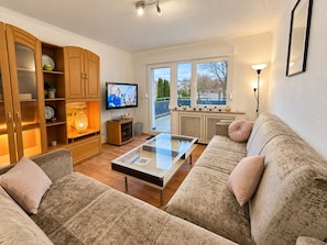 A living room with a sofa set, a coffee table, a television, and a kitchen area with a window.