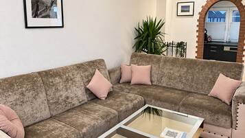 A living room with a sofa, a glass-top coffee table, and a potted plant.