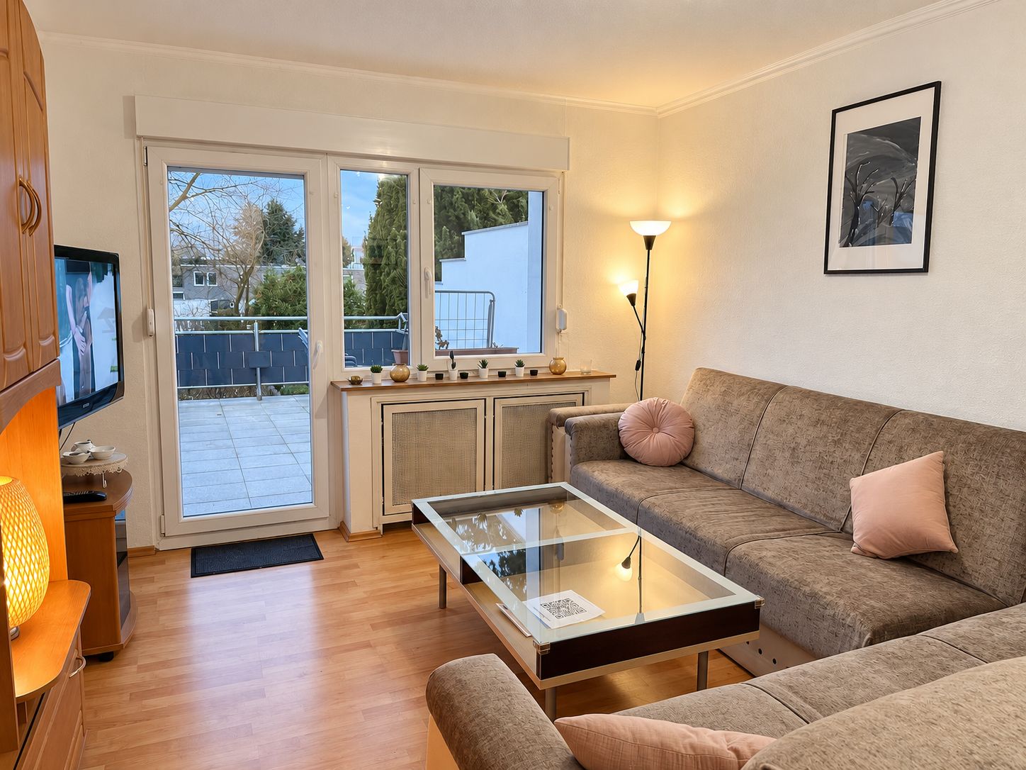 Ein Wohnzimmer mit Glastisch, einer Couch, einem Fernseher und Blick durch eine Schiebetür in einen Außenbereich.