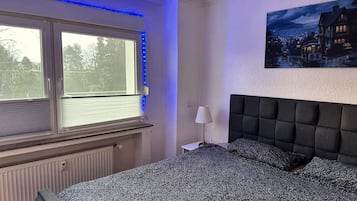 A bedroom with a large bed, a window with blinds, a radiator, and a painting on the wall.