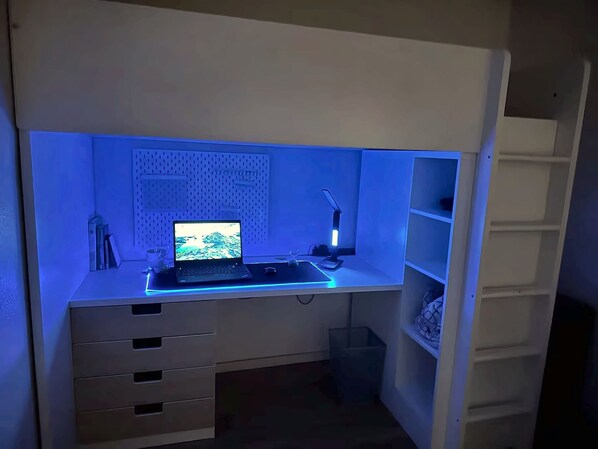 A compact workspace with a laptop, desk lamp, and shelves.