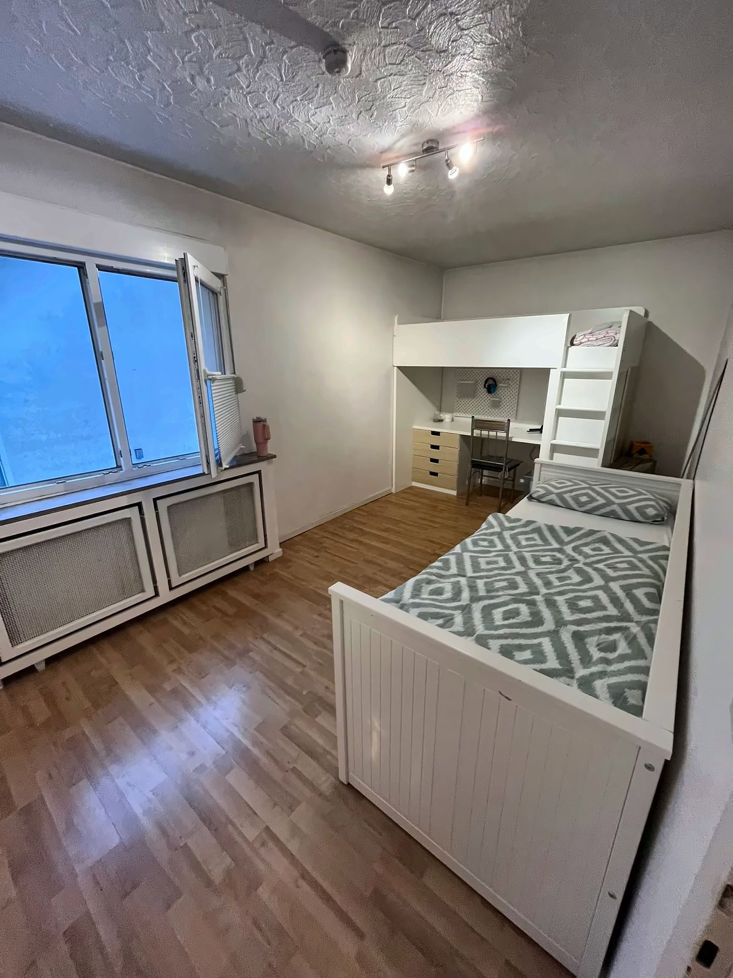 Ein Schlafzimmer mit einem Bett, einem Schreibtisch, einem Stuhl und einem Fenster.