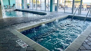 Una piscina interior con suelo de baldosas, un trampolín y sillas de descanso fuera de las ventanas.