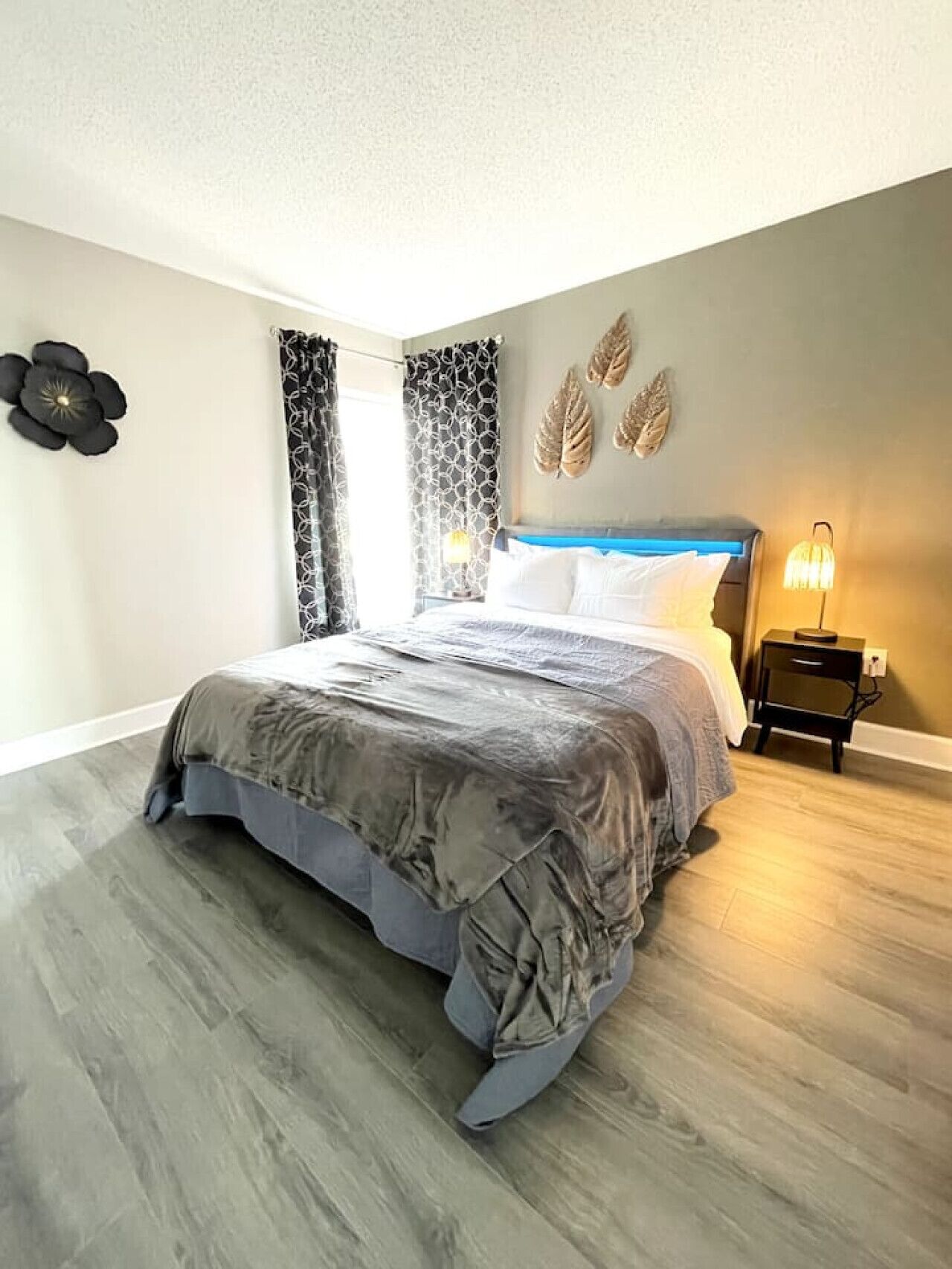A bedroom with a bed, curtains, a wall clock, and a nightstand with a lamp.
