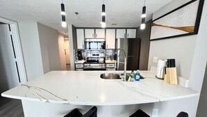 Una cocina moderna con una isla central, electrodomésticos de acero inoxidable y taburetes negros.