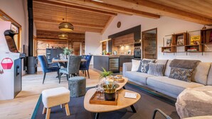 A modern living room with a sofa, coffee table, and chairs. There is a kitchen area with a refrigerator and a stove. - Le Primpiolet - Penthouse for 9 with Mont Blanc view - OVO Network (Combloux)