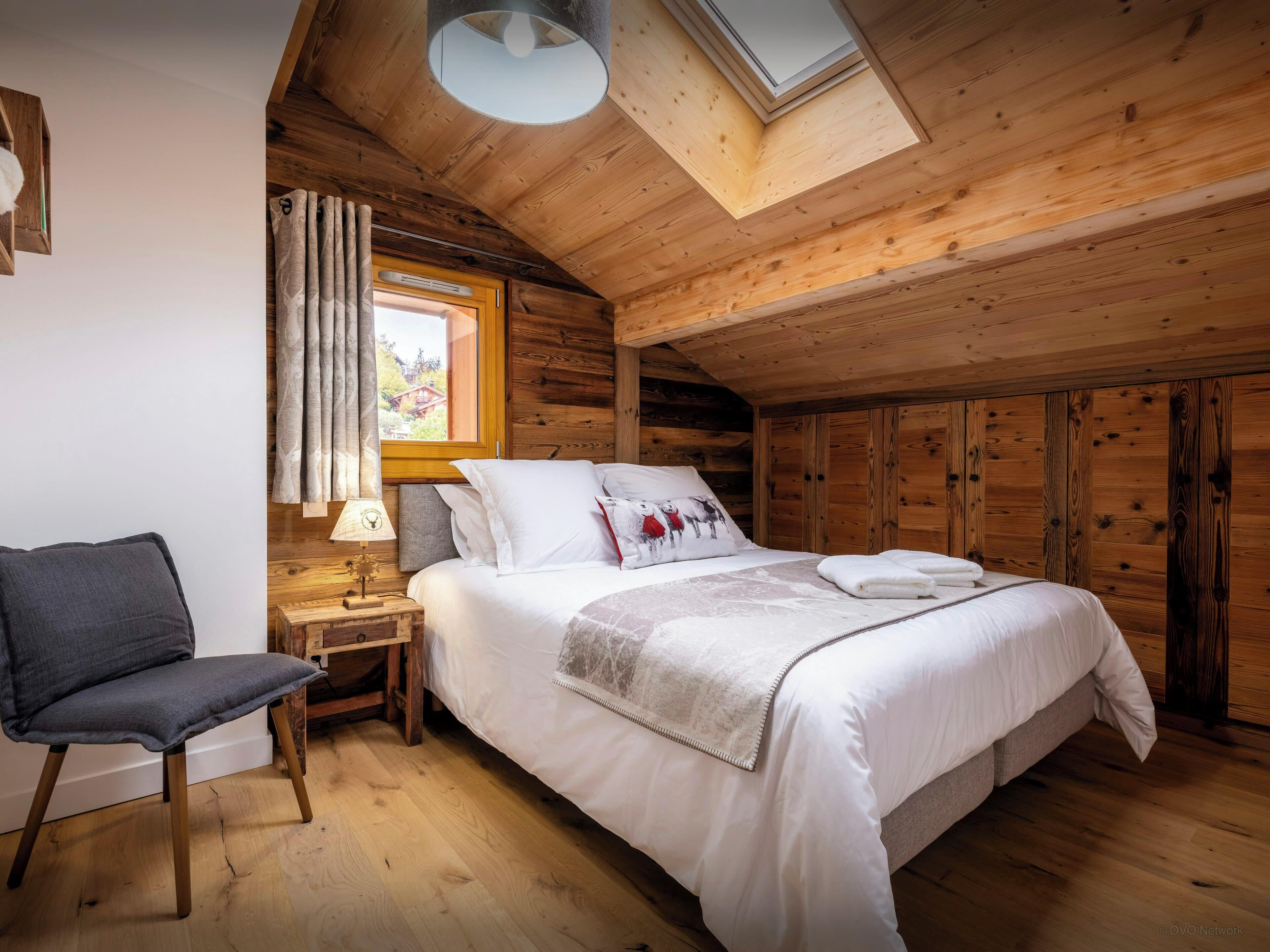 Une chambre confortable, aménagée dans un chalet en bois, avec un lit, une chaise, une table de chevet et une lucarne.