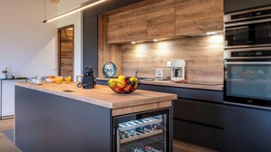 A modern kitchen with a wooden island, built-in appliances, and a wine cooler. - Le Primpiolet - Penthouse for 9 with Mont Blanc view - OVO Network (Combloux)
