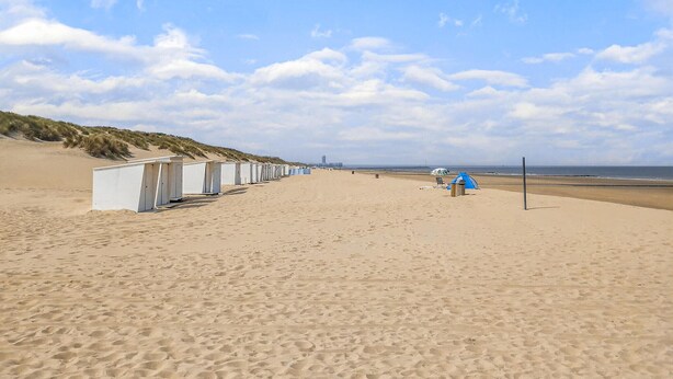 Une plage bordée de rangées de cabanes de plage blanches et de quelques tentes.