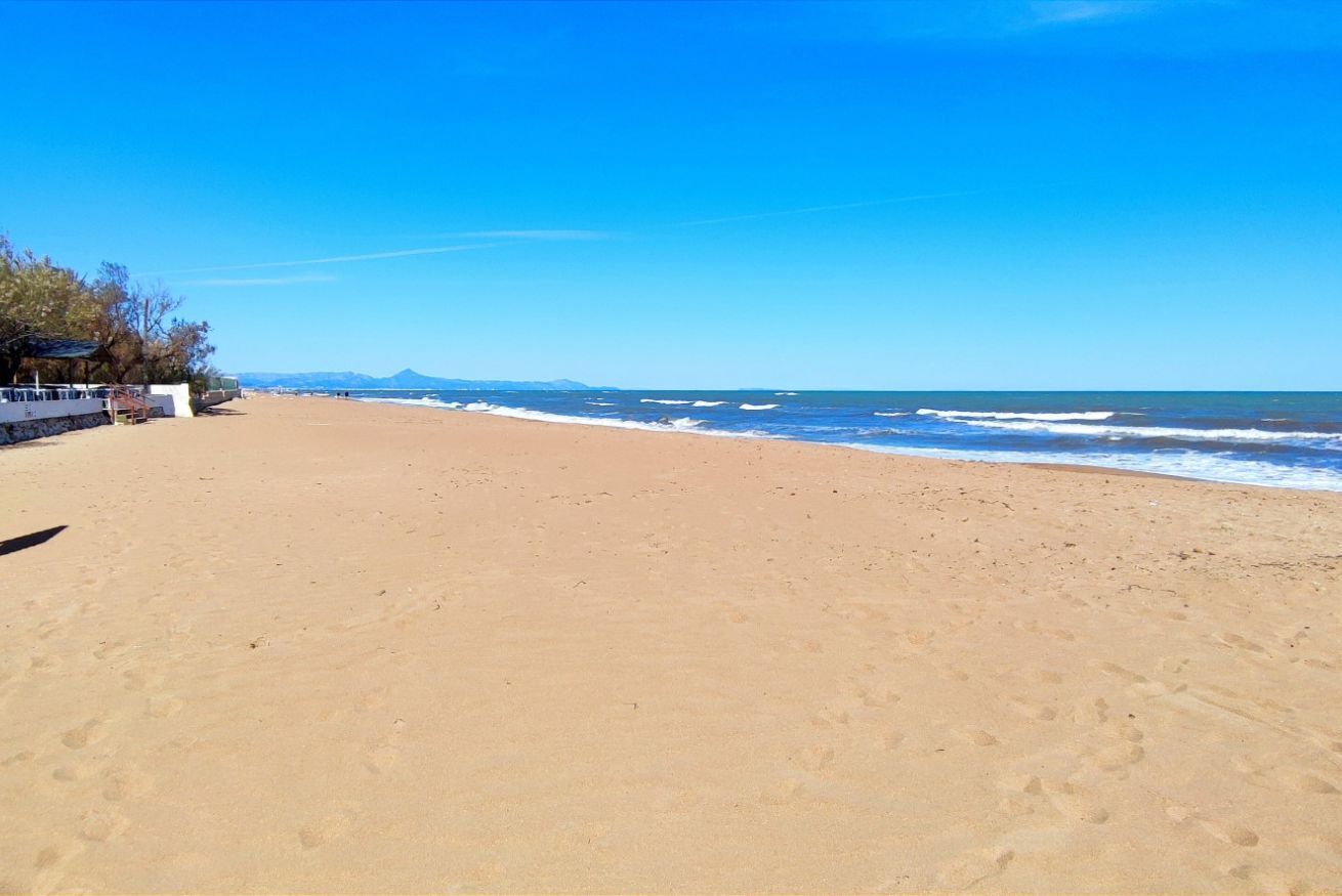 A beach with a clear sky, a sandy shore, and a distant mountain range.