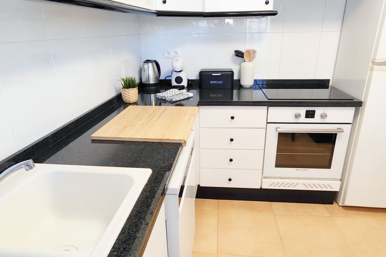 A modern kitchen with a white sink, black countertop, and a built-in oven.