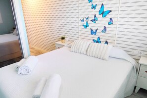 A hotel room with a bed, white linens, a nightstand with a plant, and a wall with butterfly decals. - Apartament Mar de Denia by DENIA COSTA (Dénia)