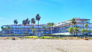 Ein Hotel direkt am Strand mit mehreren Etagen, Palmen und wolkenlosem, blauem Himmel.