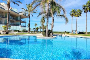 A swimming pool with a tiled border, surrounded by palm trees and a multi-story building with balconies. - Apartament Mar de Denia by DENIA COSTA (Dénia)