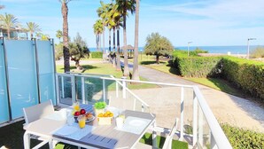 Ein Balkon mit Frühstückstisch, mit Blick auf einen Garten mit Palmen und Meer.