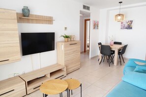 Un salon moderne doté d’un téléviseur à écran plat, de meubles en bois, d’un coin repas avec des chaises et d’un canapé bleu.