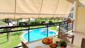 Un balcón con vista a la piscina, una mesa con frutas y jugo, y una planta en maceta.