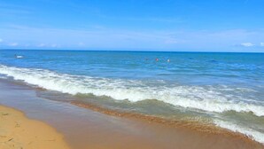 Una playa con aguas azules transparentes, una orilla de arena y algunas personas a lo lejos.
