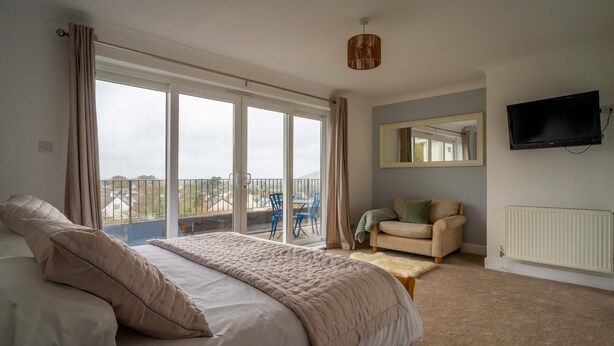A bedroom with a large bed, a sofa, a chair, a television, and a view of the outside. - Croft House  -  a house  that sleeps 10 guests  in 5 bedrooms (Croyde Braunton)