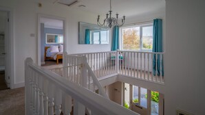A spacious room with a balcony, a chandelier, and a large window with curtains. - Croft House  -  a house  that sleeps 10 guests  in 5 bedrooms (Croyde Braunton)