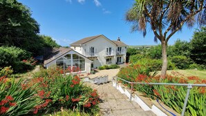 A two-story house with a balcony, surrounded by lush greenery and flowering plants. - Croft House  -  a house  that sleeps 10 guests  in 5 bedrooms (Croyde Braunton)