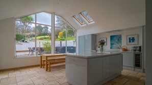 A modern kitchen with large windows, a central island, and a view of the garden. - Croft House  -  a house  that sleeps 10 guests  in 5 bedrooms (Croyde Braunton)
