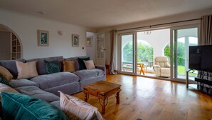 A living room with a sectional sofa, a wooden coffee table, a TV, and a sliding glass door leading to an outdoor patio. - Croft House  -  a house  that sleeps 10 guests  in 5 bedrooms (Croyde Braunton)
