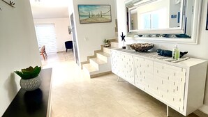 Um interior moderno com uma escadaria que leva a outro nível, uma mesa consola branca com objetos decorativos e um espelho grande em cima.