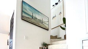 Uma escadaria moderna com design minimalista, uma pintura de uma paisagem costeira e um vaso de planta no patamar.
