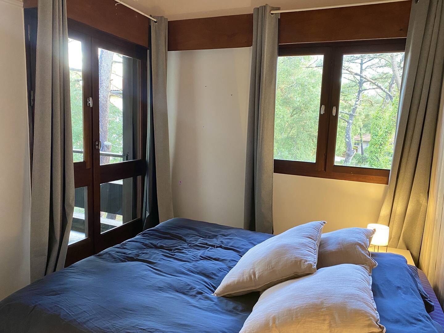 A bedroom with a bed, curtains, and a window with a view of trees.
