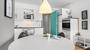 Una cucina moderna con mobili bianchi, forno a microonde integrato, lavastoviglie e un tavolo rotondo grande con una rivista e una tazza da caffè.