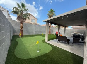 A backyard with artificial grass, a barbecue area, and a covered seating area. - 3BR Vegas Home • Near the Strip, Allegiant & Airport • Sleeps 8 (Las Vegas)