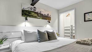 Un dormitori modern amb un llit gran, dues làmpades de nit, un quadre d'un paisatge de muntanya i una porta que dona a un bany.