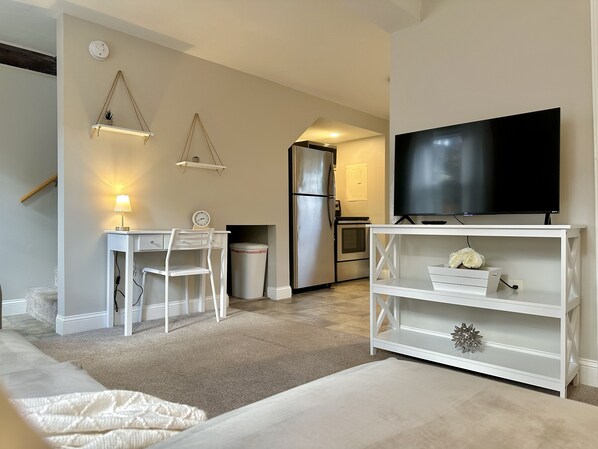 A compact living space with a kitchenette, a dining area with a table and chairs, a TV on a white stand, and a small shelf with decorative items. - New, Clean, Downtown Getaway! (Concord)