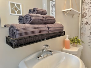 A bathroom with a sink, a mirror, and a towel rack holding rolled towels. - New, Clean, Downtown Getaway! (Concord)