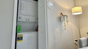 A laundry room with a washing machine, a wall-mounted lamp, and a small plant. - New, Clean, Downtown Getaway! (Concord)