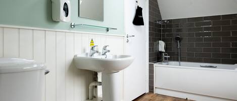 Une salle de bain avec un lavabo, un miroir et des toilettes blancs, un espace de douche noir et un revêtement de sol en bois.