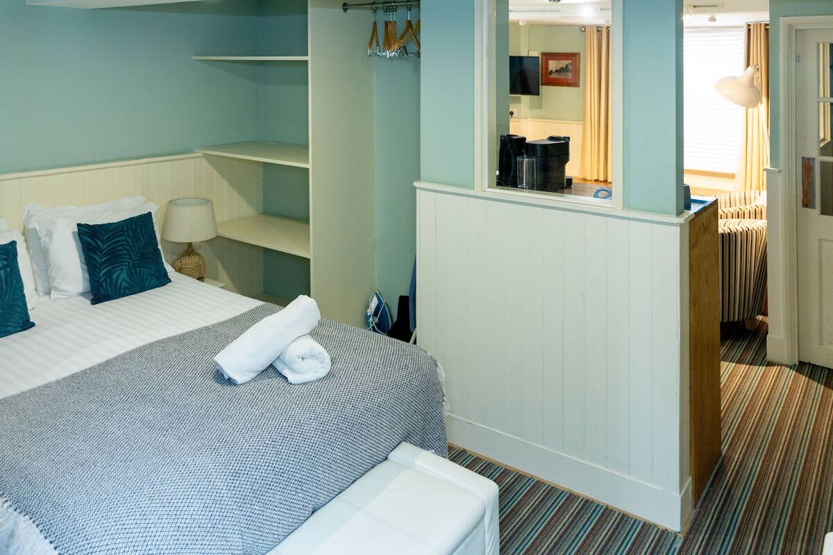 A hotel room with a bed, a small desk, a mirror, and a bathroom visible through an open door.