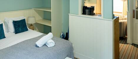 A hotel room with a bed, a small desk, a mirror, and a bathroom visible through an open door.