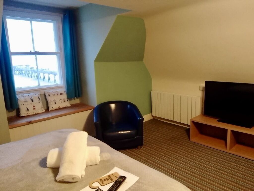 Ein Hotelzimmer mit Bett, Sessel, Fernseher und einem Fenster mit Vorhängen.