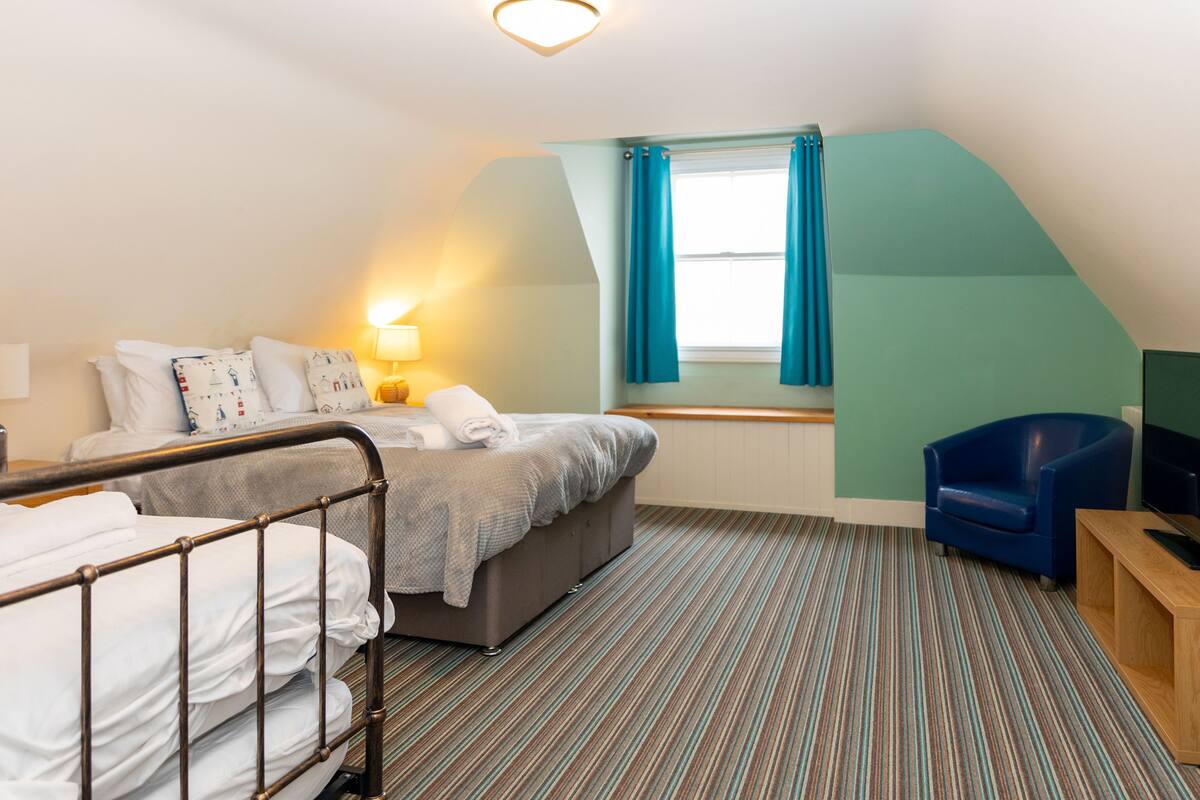 A hotel room with a bed, a chair, a TV, and a window with curtains.