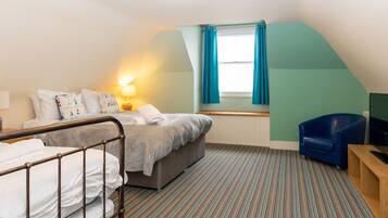 A hotel room with a bed, a chair, a TV, and a window with curtains.