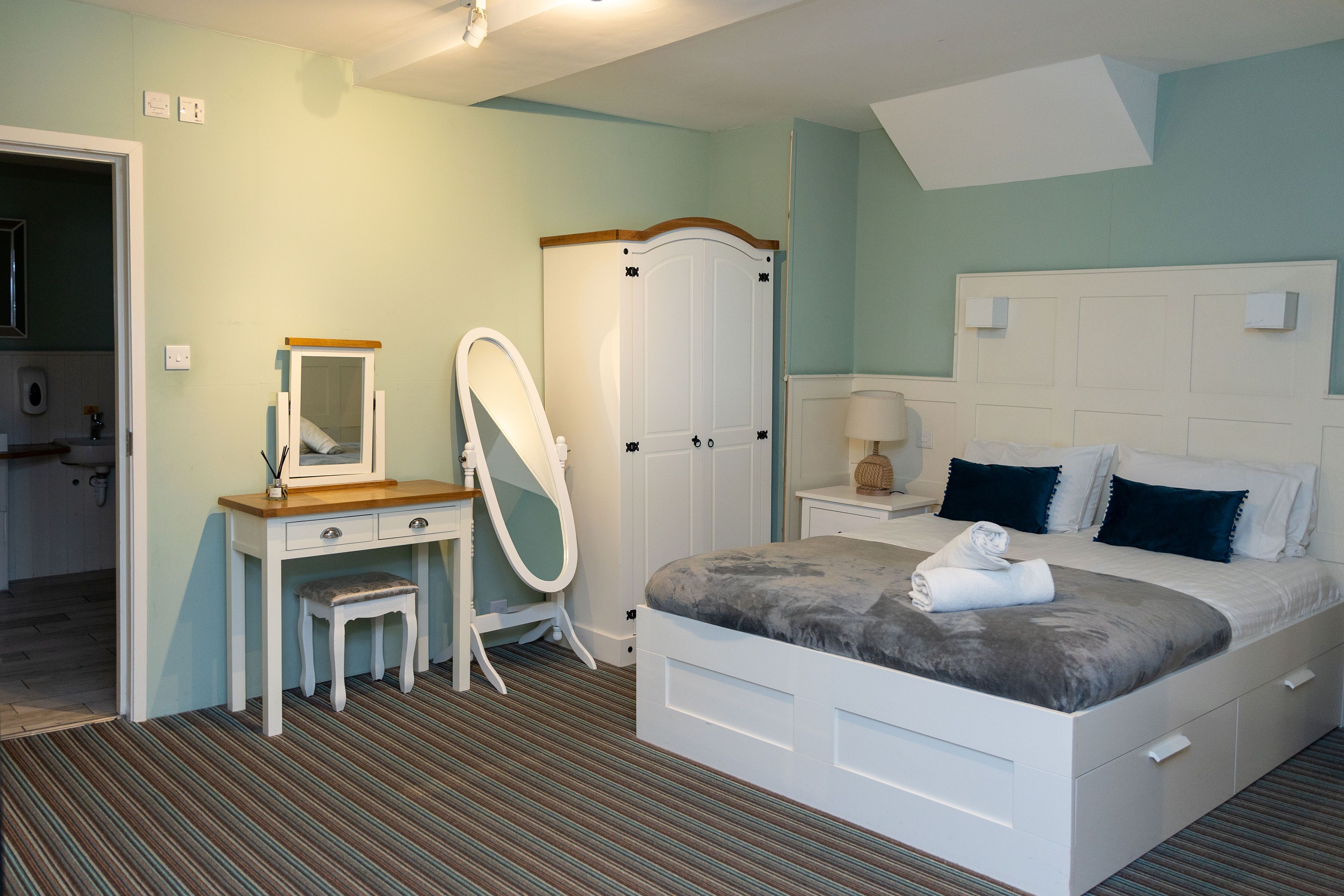 Een slaapkamer met een bed, een dressoir, een kaptafel met spiegel en een garderobe.