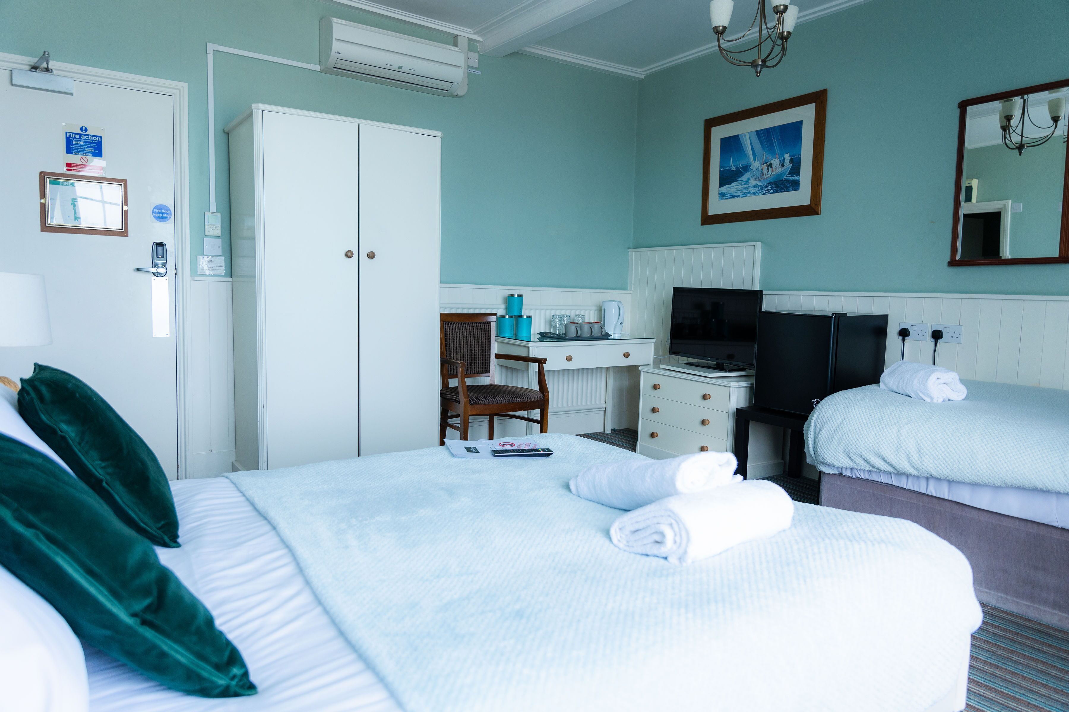 A hotel room with two beds, a desk with a computer, a TV, and a painting on the wall.